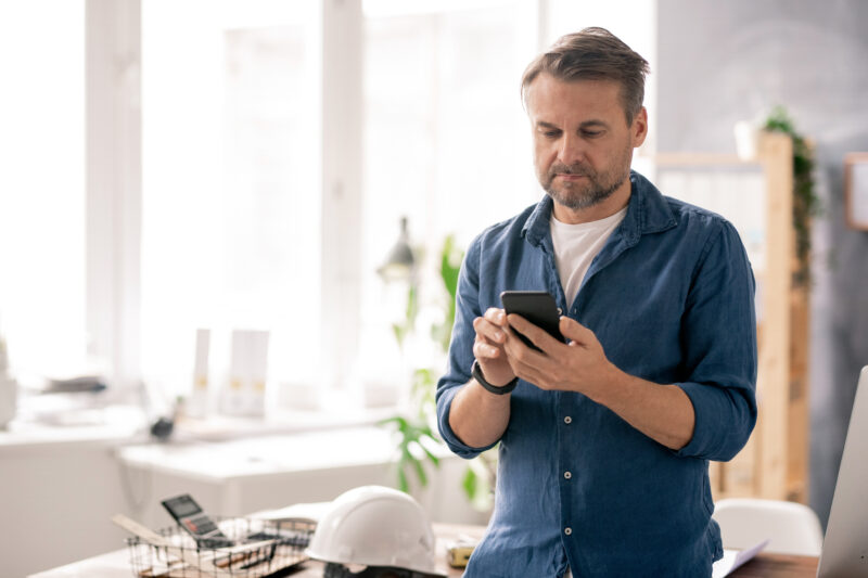 Serious,Engineer,In,Casualwear,Scrolling,Through,Contacts,In,His,Smartphone