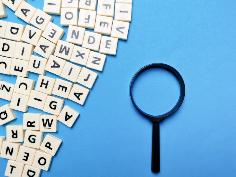 Square,Letter,Tiles,With,Magnifying,Glass,Against,Blue,Background.,Search
